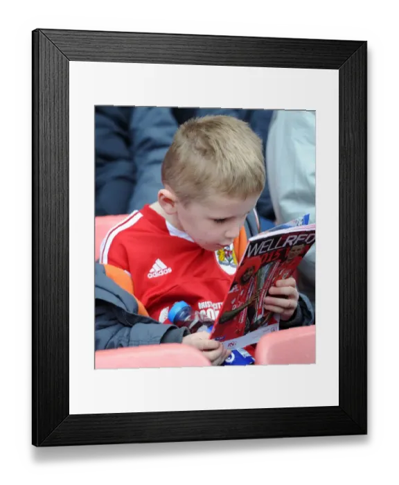 Framed Print : Young Fan Examines Match Program at Bristol City vs Barnsley Game, March 2015